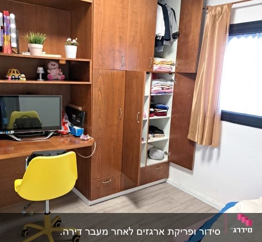 חדר עם ארון בגדים פתוח, מדפים עם חפצים, כיסא צהוב ושולחן עבודה.